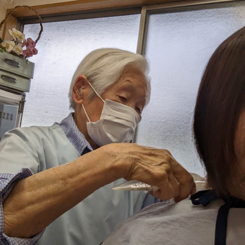 Her well-developed arm muscles are visible while she cuts the hair of LongeviQuest Japan President Yumi Yamamoto (photo taken June 6, 2023)