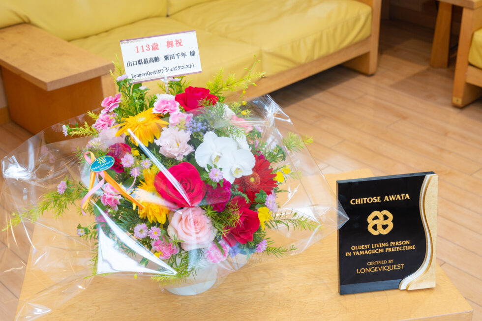 粟田千年さんに贈られた花とLongeviQuestの記念楯